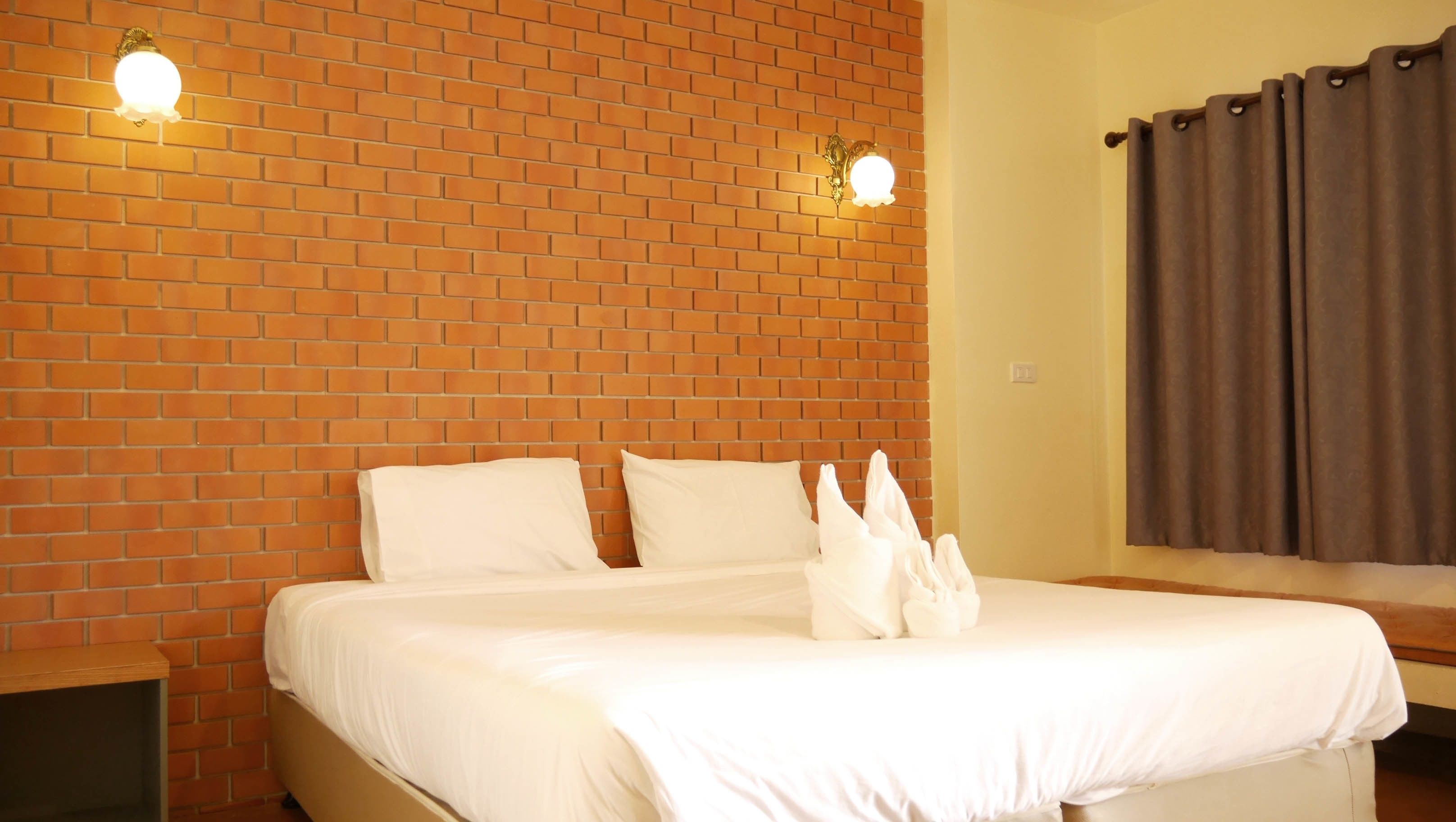 A hotel room with a brick wall, a bed with white bedding, and two wall-mounted lights.