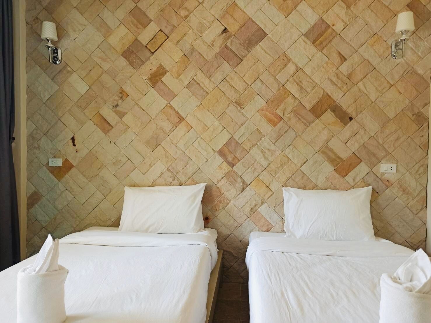 A hotel room with two beds, a herringbone-patterned wall, and two wall-mounted lamps.