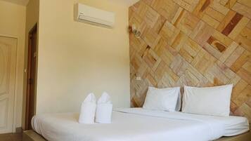 Habitación de hotel con cama, ropa de cama blanca, cabecera de madera, unidad de aire acondicionado y una puerta.