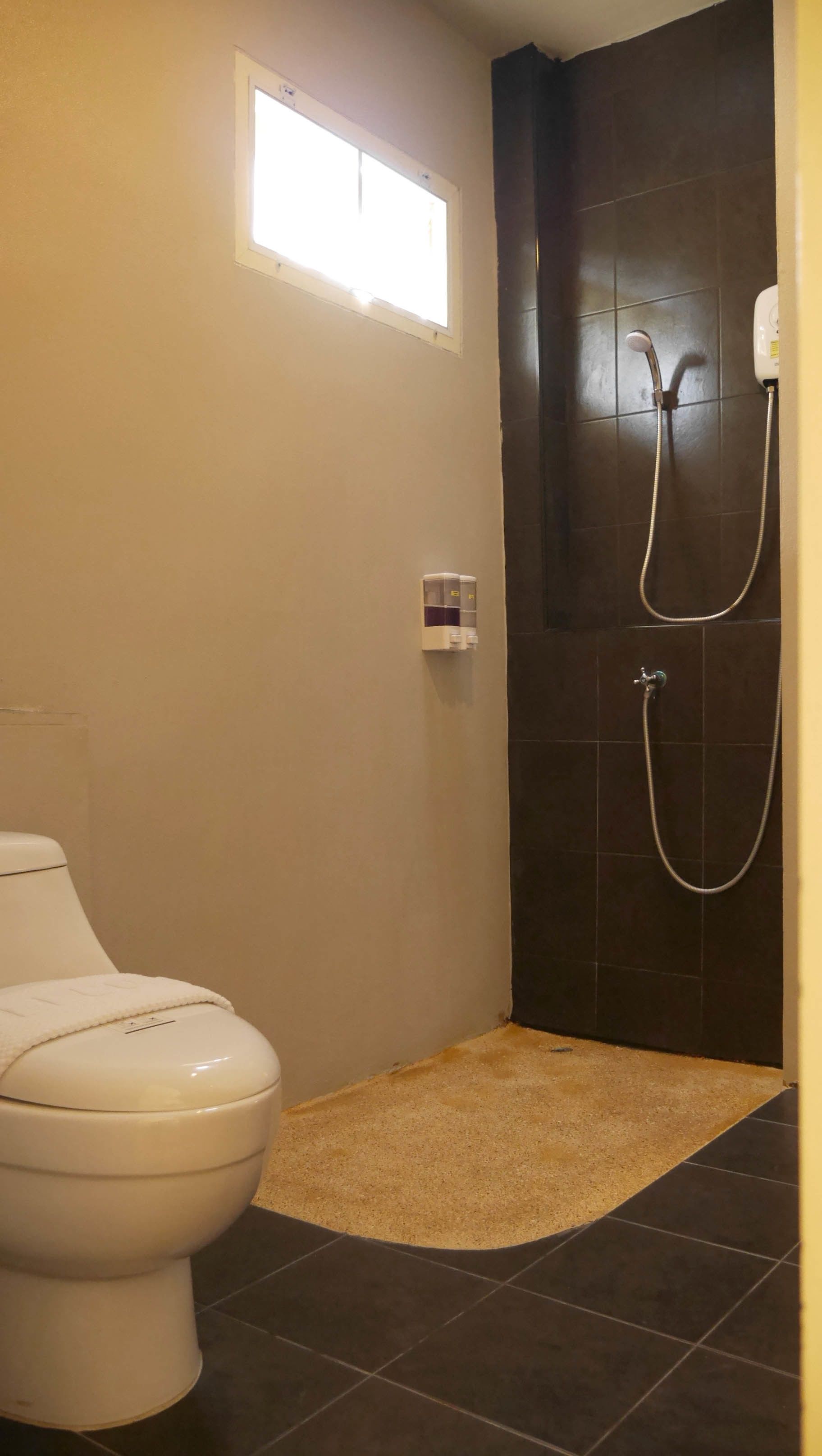 Un baño con inodoro, ducha y un ventanal pequeño.