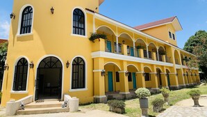 Un edificio amarillo con varios ventanales arqueados y un corredor cubierto.