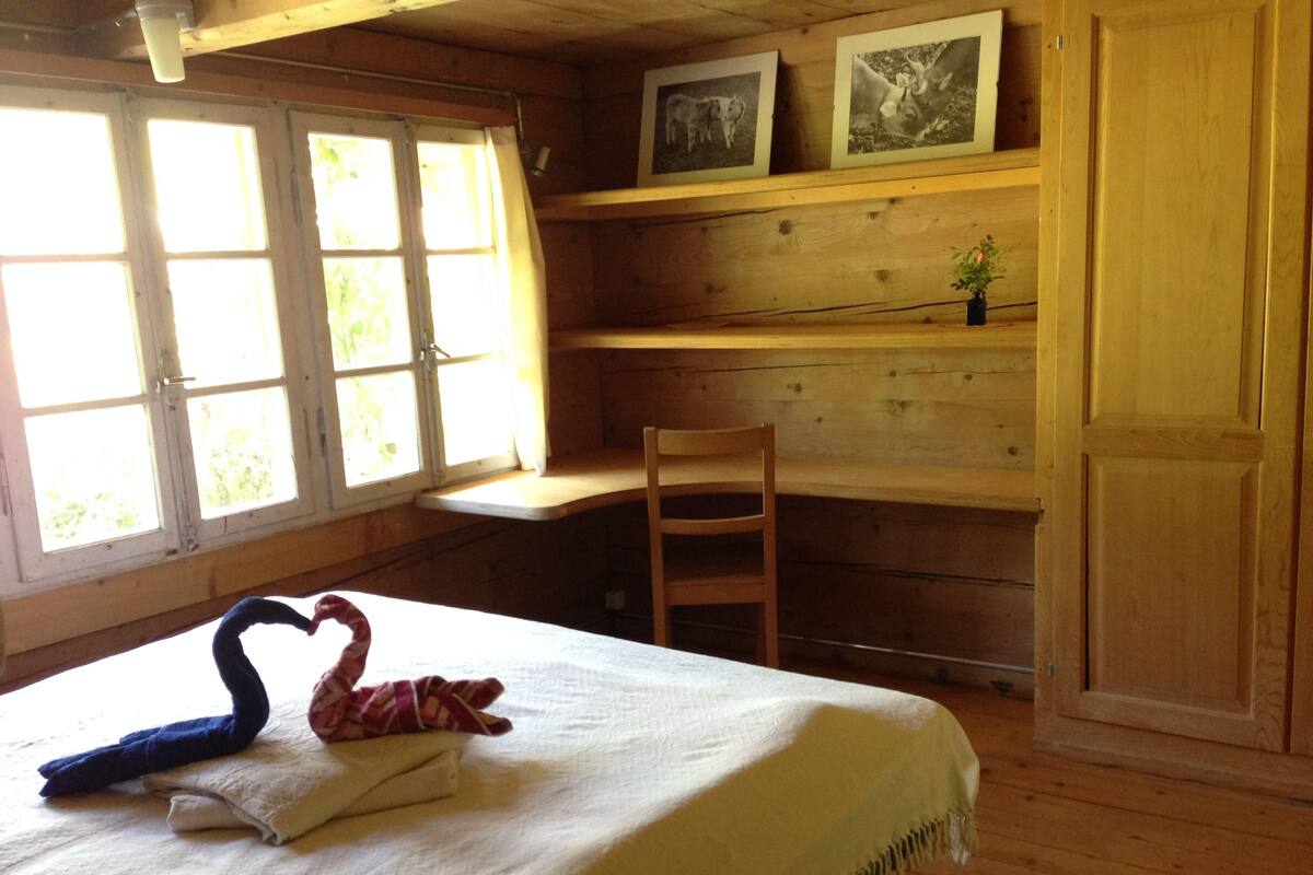 Una habitación de cabaña de madera con una cama, una silla y una estantería con fotografías enmarcadas.