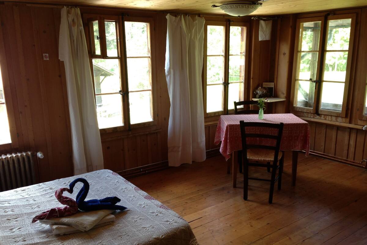 Una habitación de madera con una cama, una mesa con mantel y una silla.