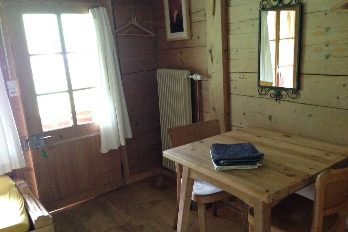 Una habitación de madera con una mesa, sillas, un radiador, un espejo y una ventana con cortinas.