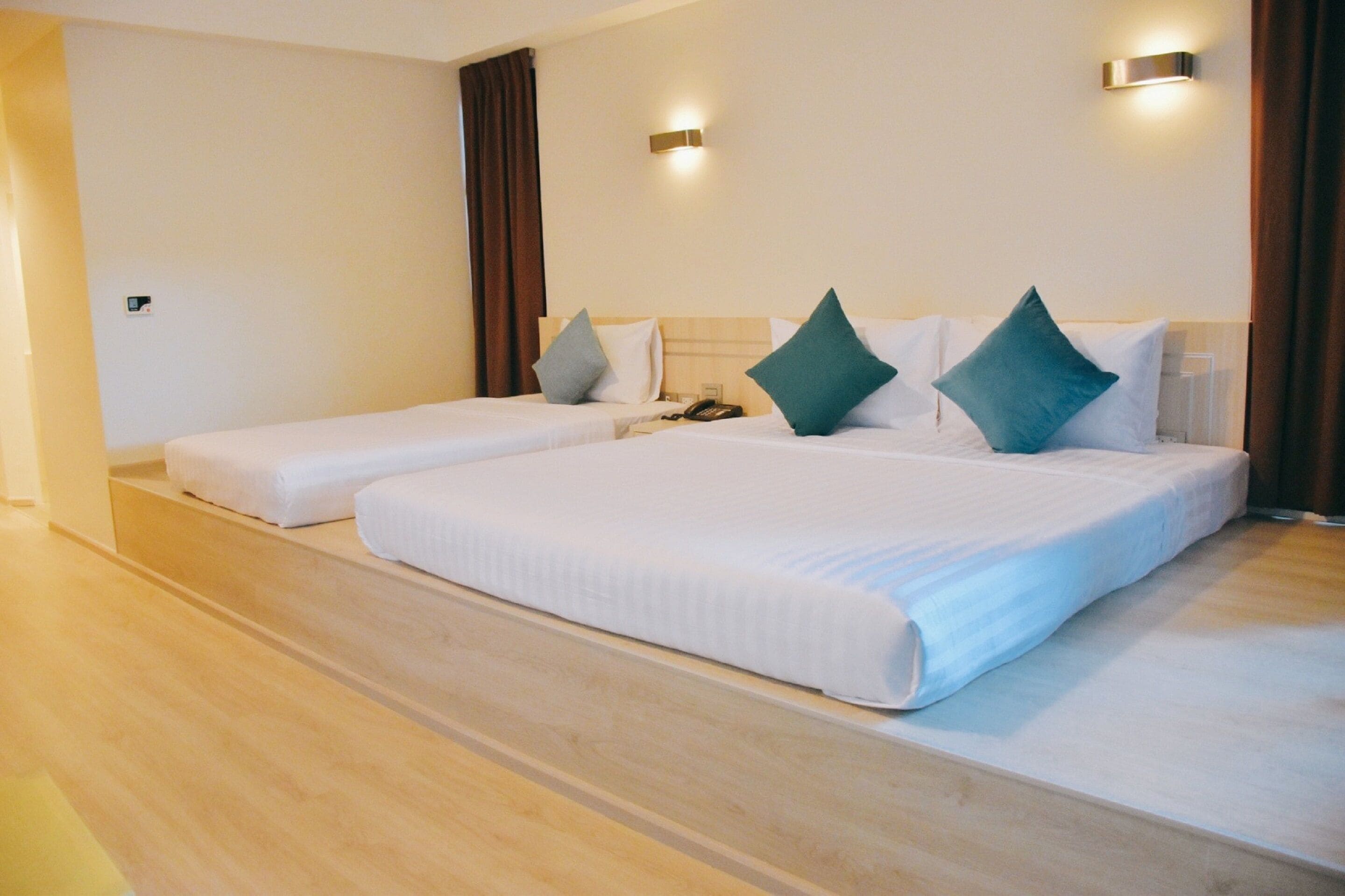 Ein Hotelzimmer mit zwei Einzelbetten, Holzboden und einer Wandleuchte.