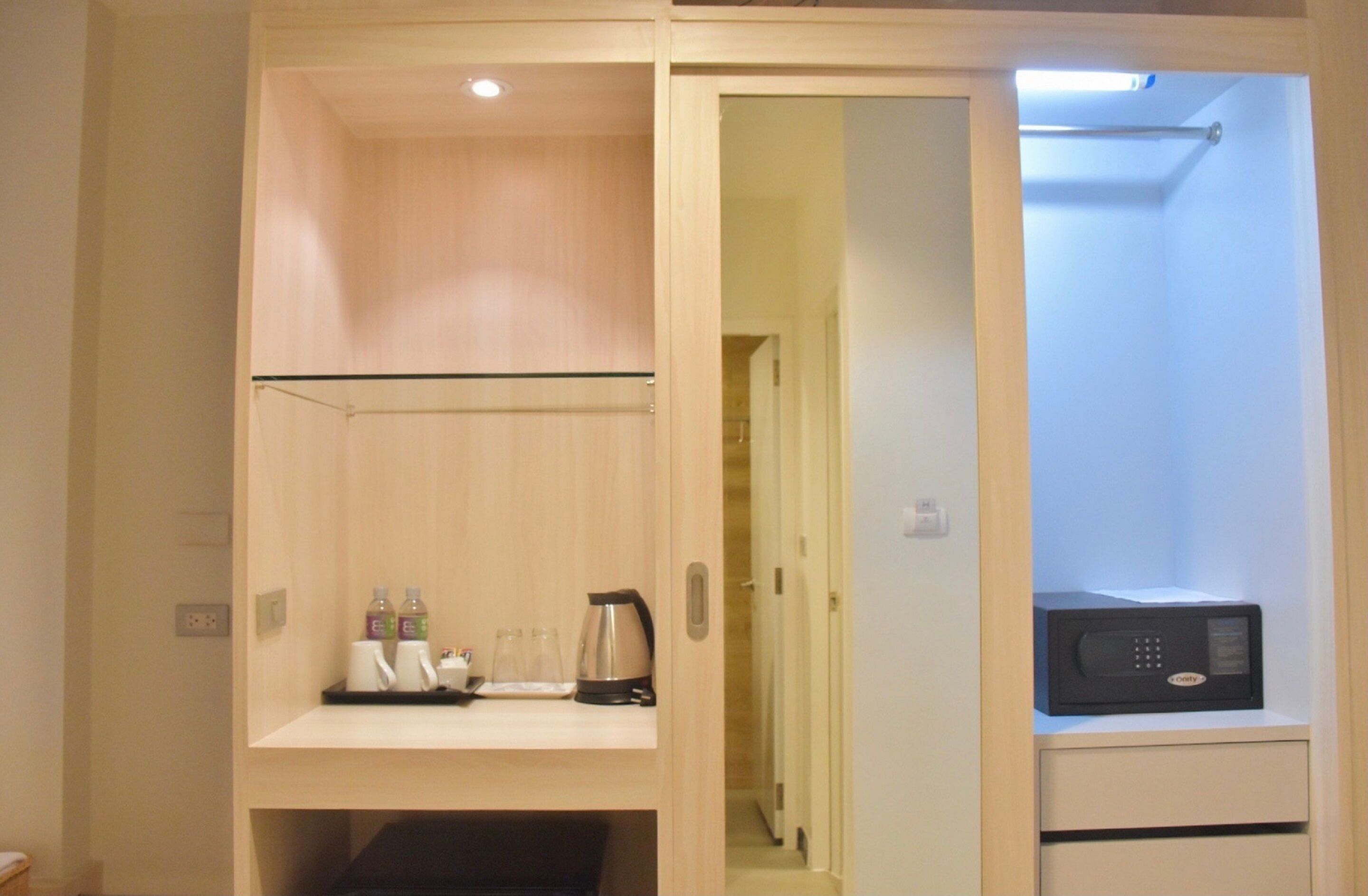 Habitación de hotel con un armario de madera, microondas, tetera y repisas con artículos de aseo.