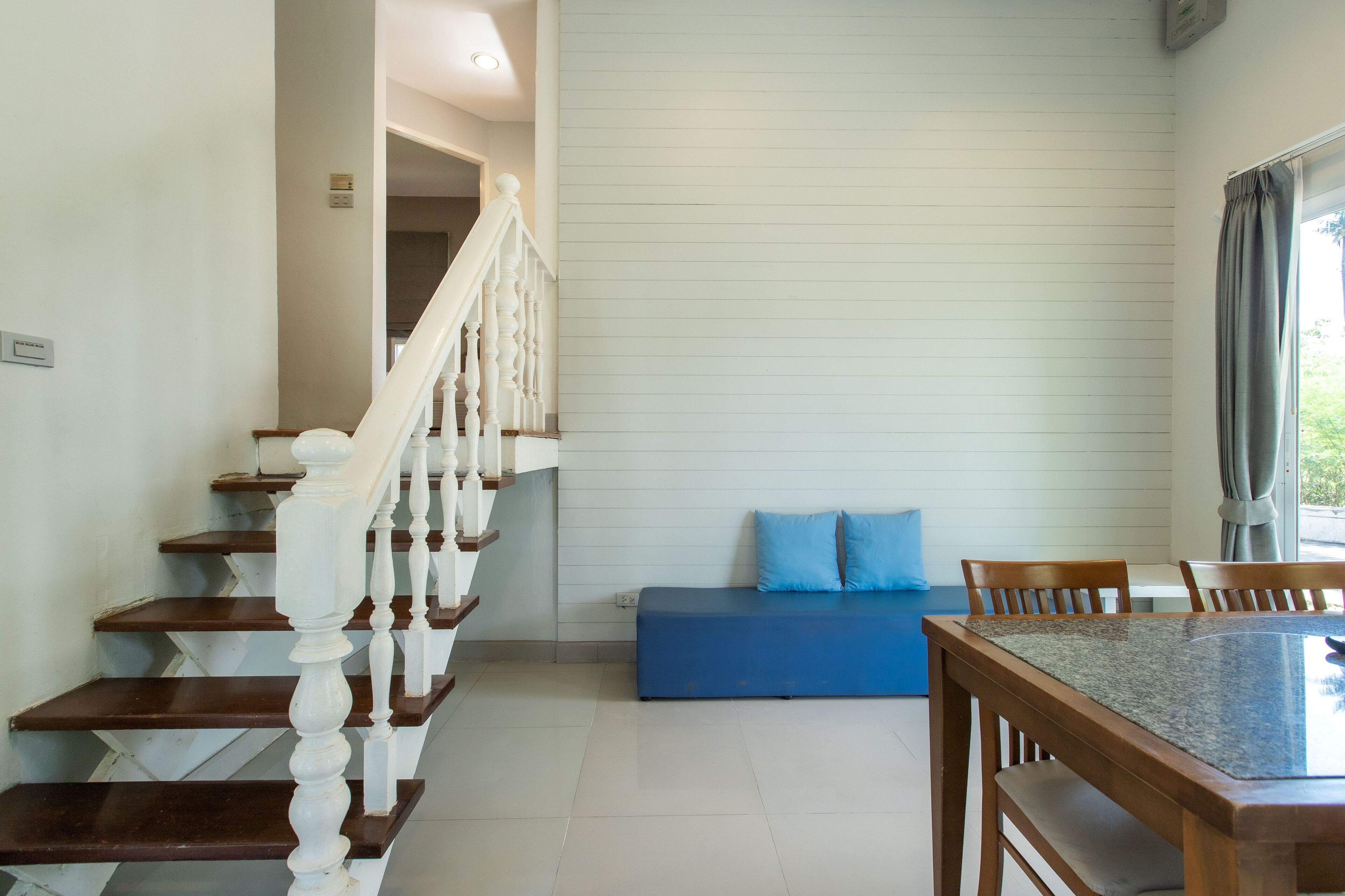 Una escalera con barandillas blancas, un sofá azul y una mesa de comedor con sillas.