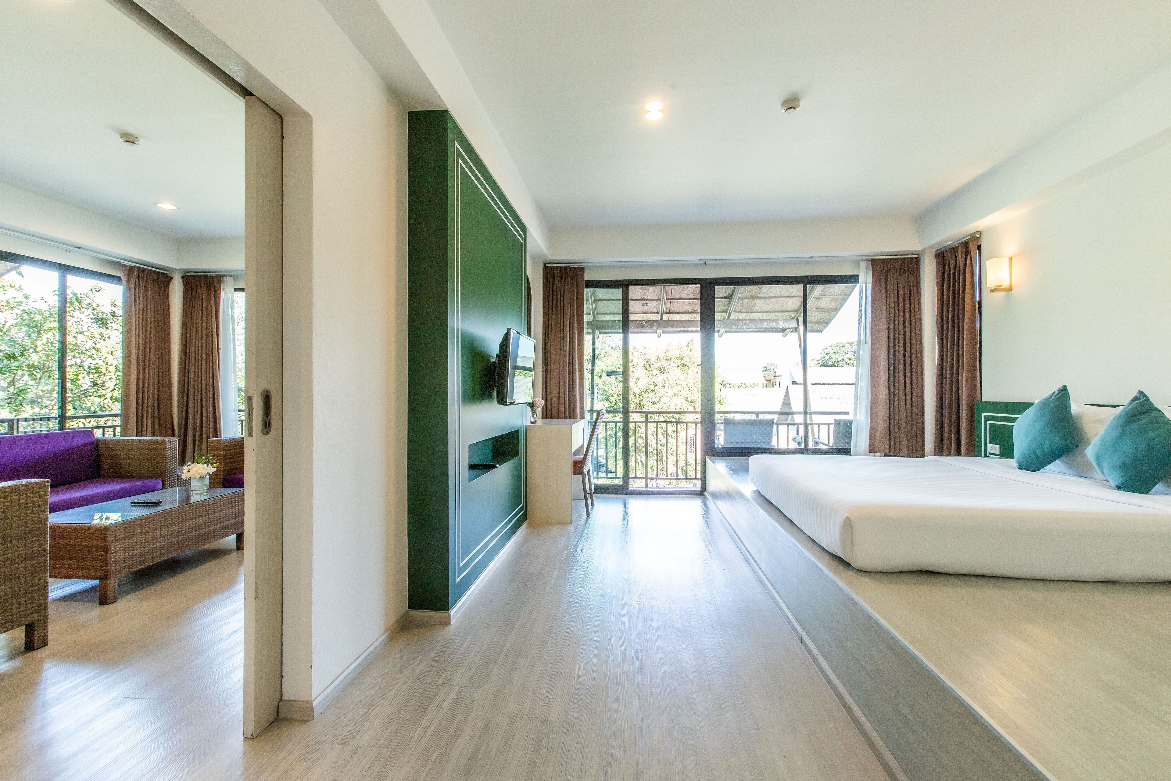 A modern hotel room with a balcony, a sofa, a TV, and a dining area.