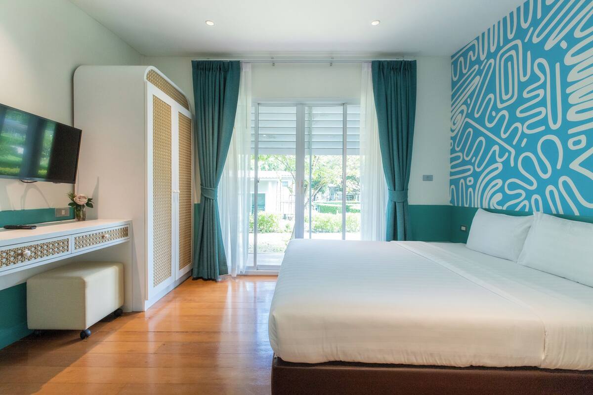Une chambre d’hôtel dotée d’un grand lit, d’un téléviseur à écran plat, d’un bureau avec un ordinateur et offrant une vue sur l’extérieur grâce à une porte coulissante.