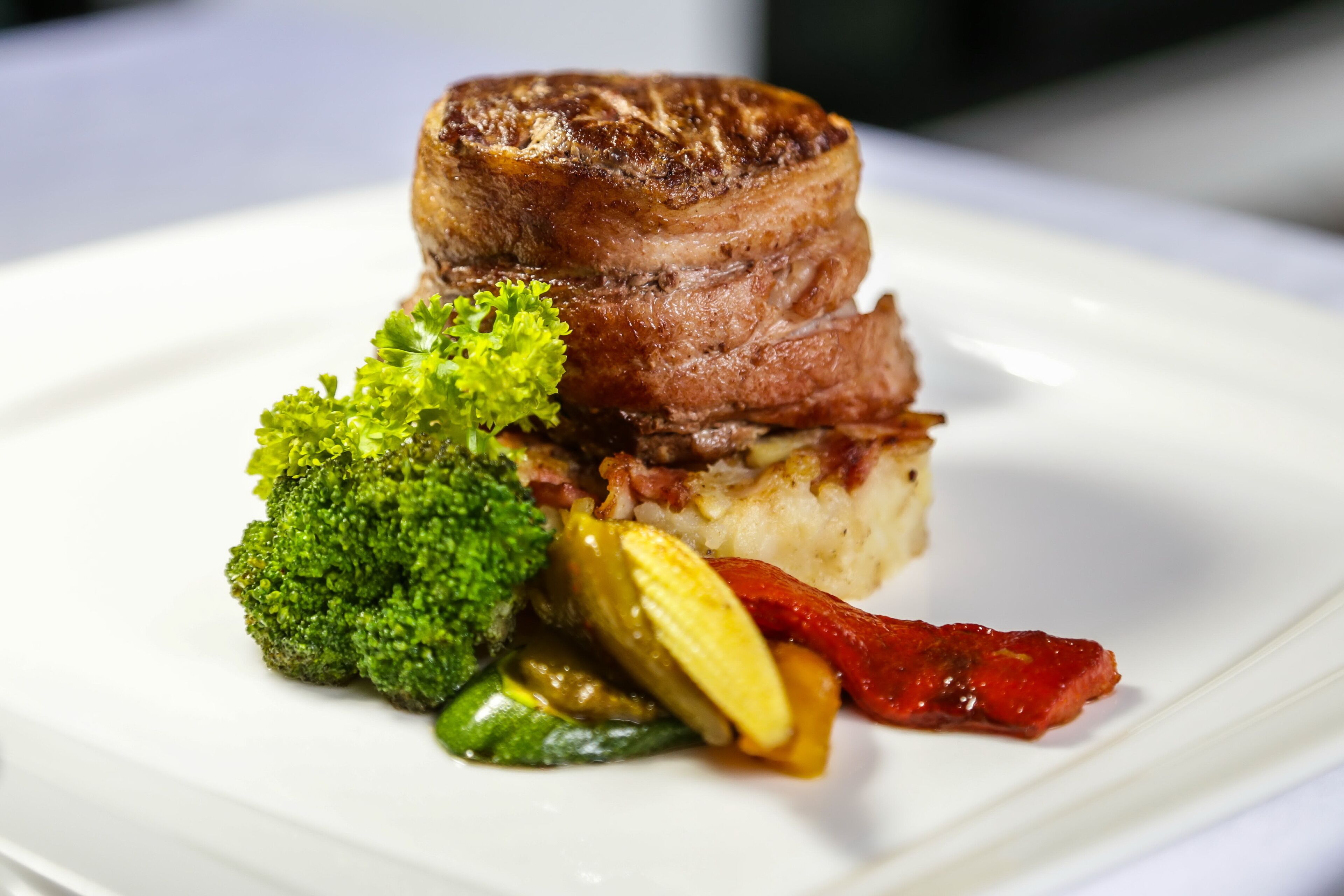 A plate with a piece of meat, broccoli, and pickles.