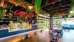 Una cafetería con techo de madera, plantas colgantes y una vitrina con postres.