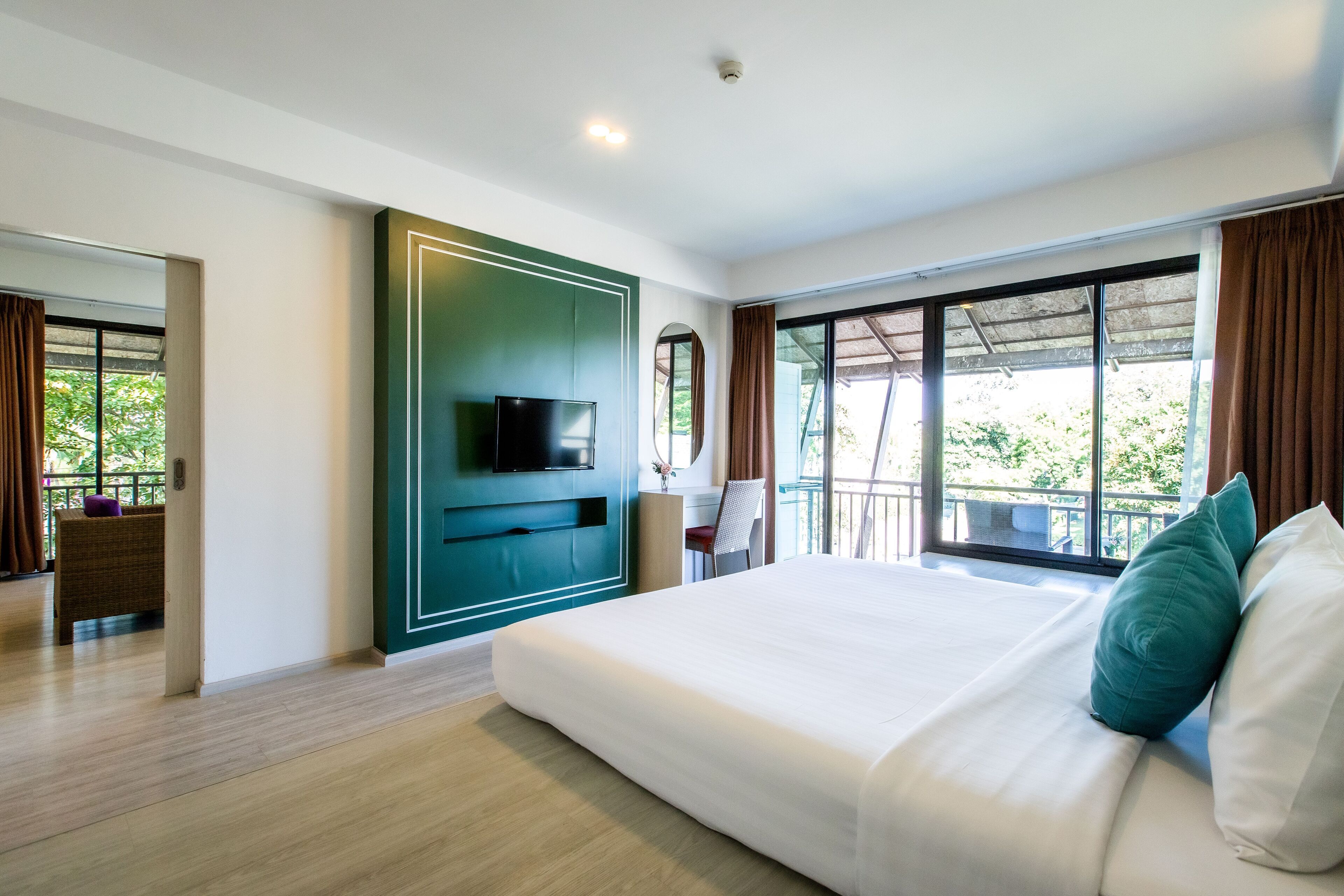 Habitación de hotel moderna con una cama grande, un televisor de pantalla plana y un balcón con vistas a zonas verdes.
