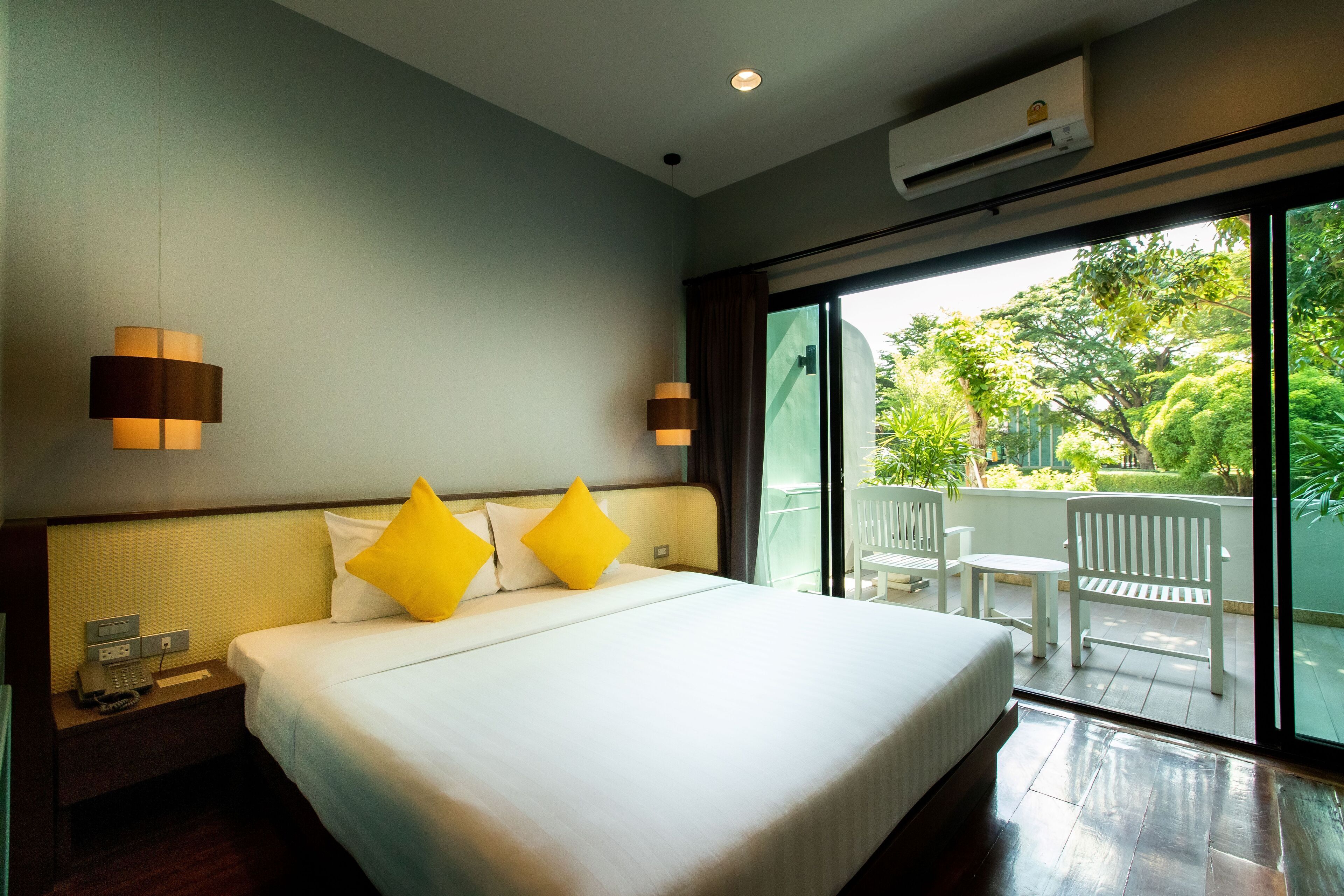Habitación de hotel con una cama grande, dos lámparas de noche, una mesita de noche con un teléfono y vistas a un balcón con mobiliario exterior.