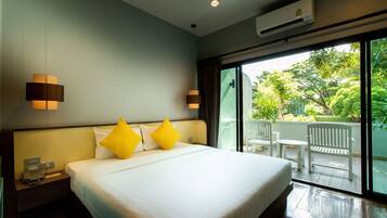 Habitación de hotel con una cama grande, dos lámparas de noche, una mesita de noche con un teléfono y vistas a un balcón con mobiliario exterior.