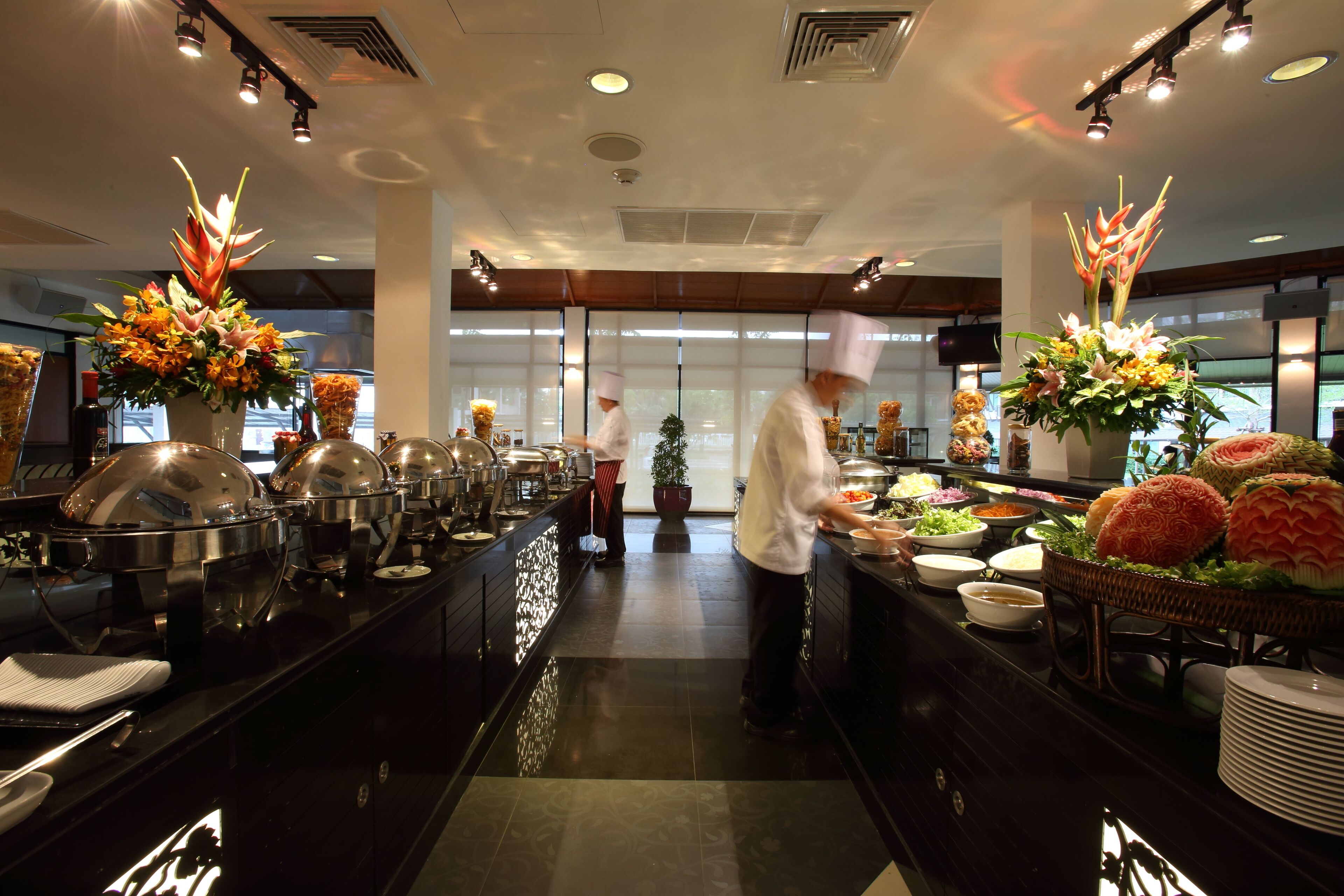 A buffet area with food stations, a potted plant, and a decorative flower arrangement.