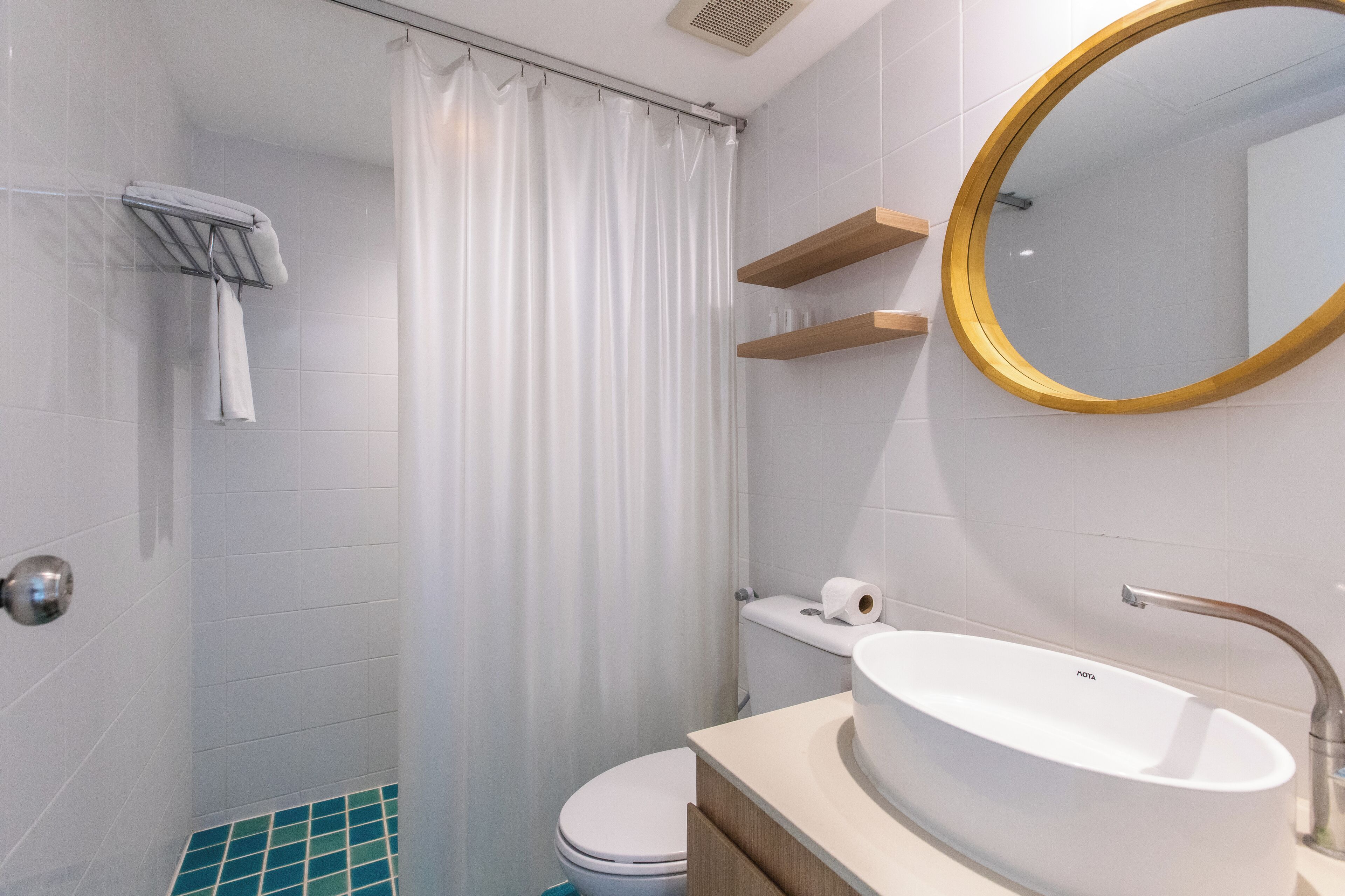 Un baño moderno con lavamanos blanco, inodoro, cortina de ducha y espejo con marco dorado.