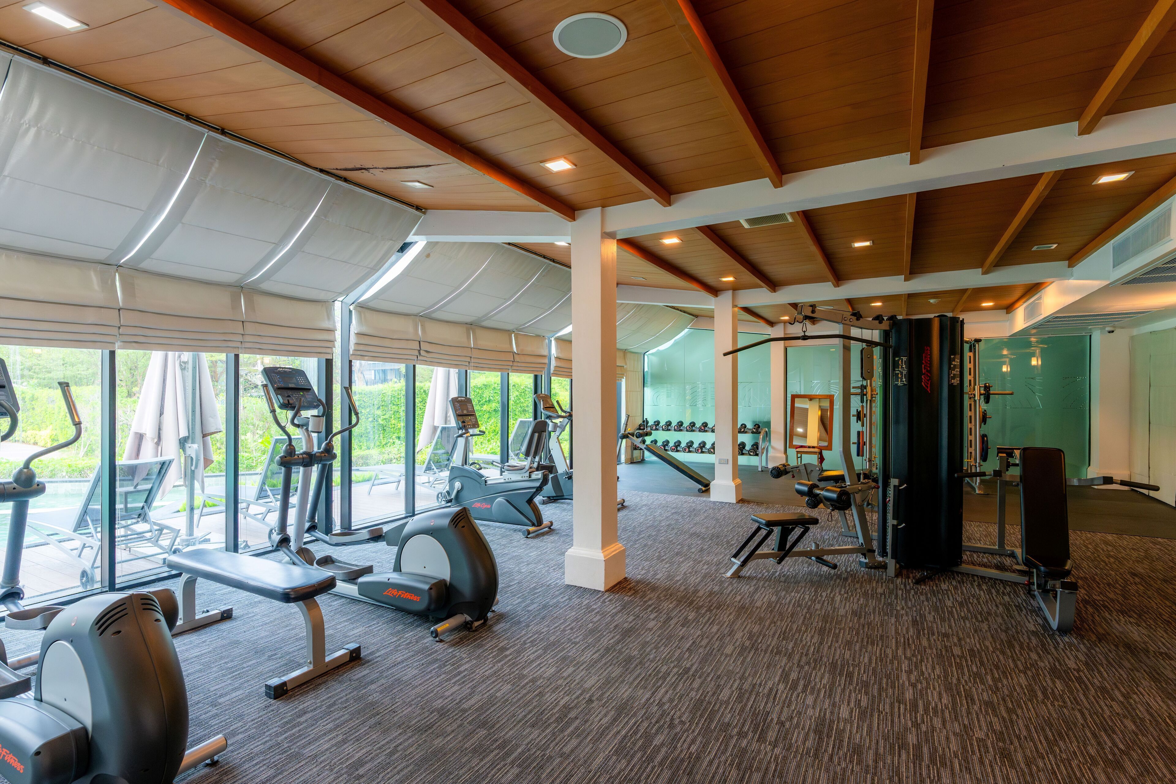 Un gimnasio con equipo de cardio, máquinas de pesas y un espejo grande.