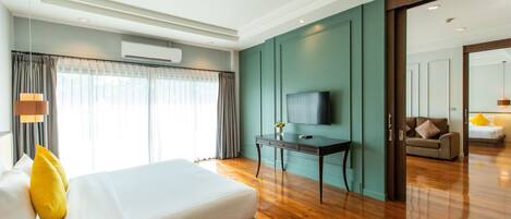 Una habitación de hotel moderna con una cama grande, un escritorio con televisor de pantalla plana y vistas al área de estar contigua.