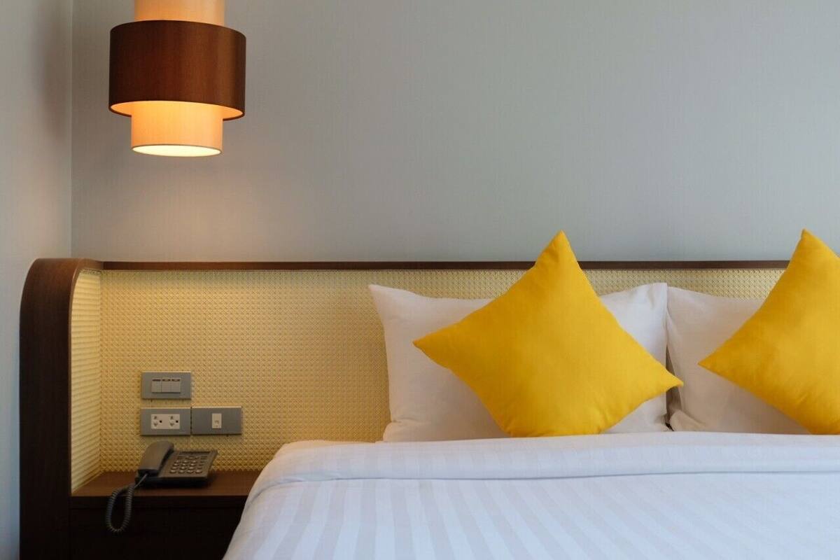 Une chambre d’hôtel avec un lit, deux oreillers jaunes, un téléphone sur la table de chevet et une lampe fixée au mur.