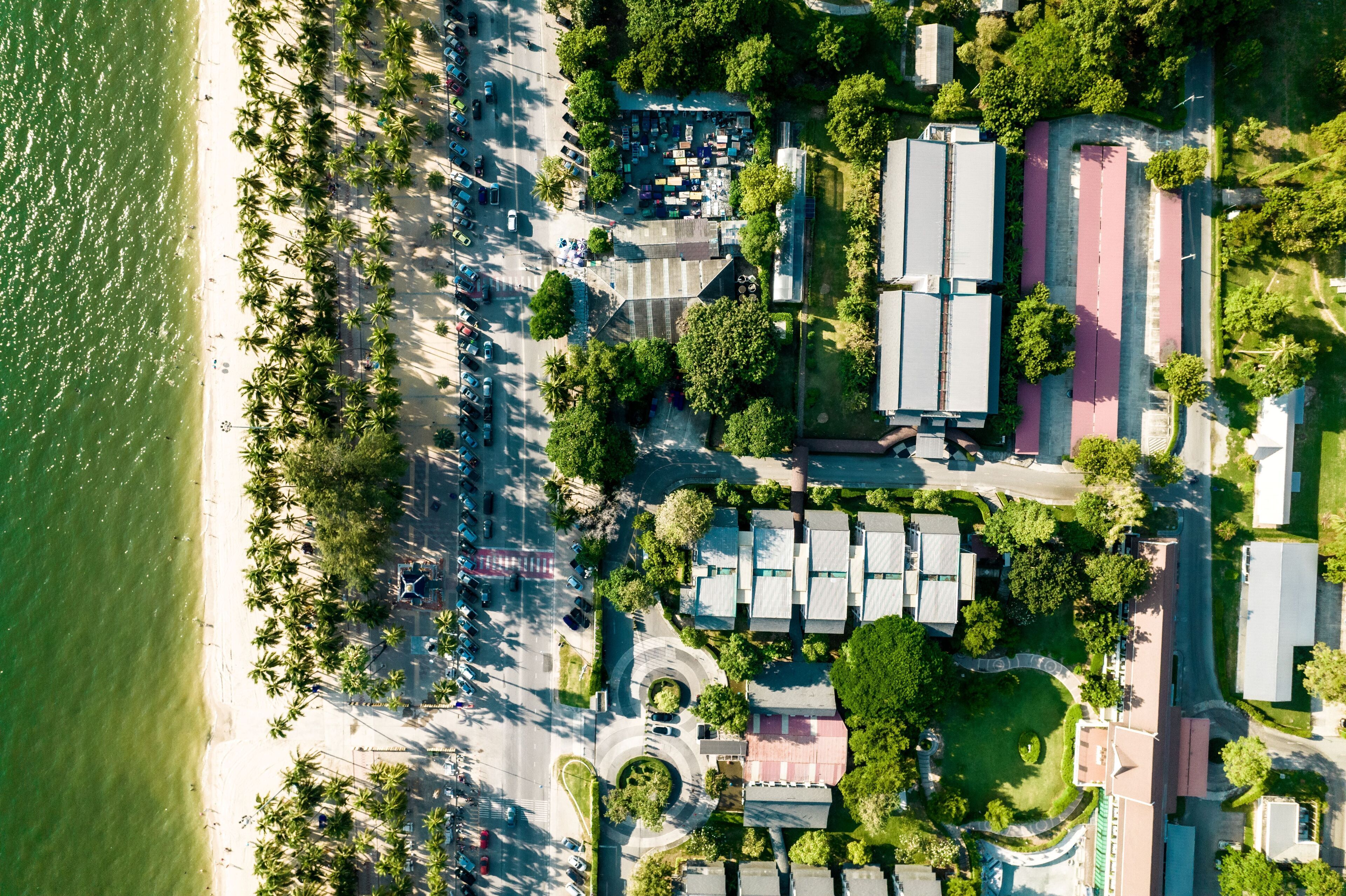 An aerial view of a coastal area with a beach, parking lots, and buildings.