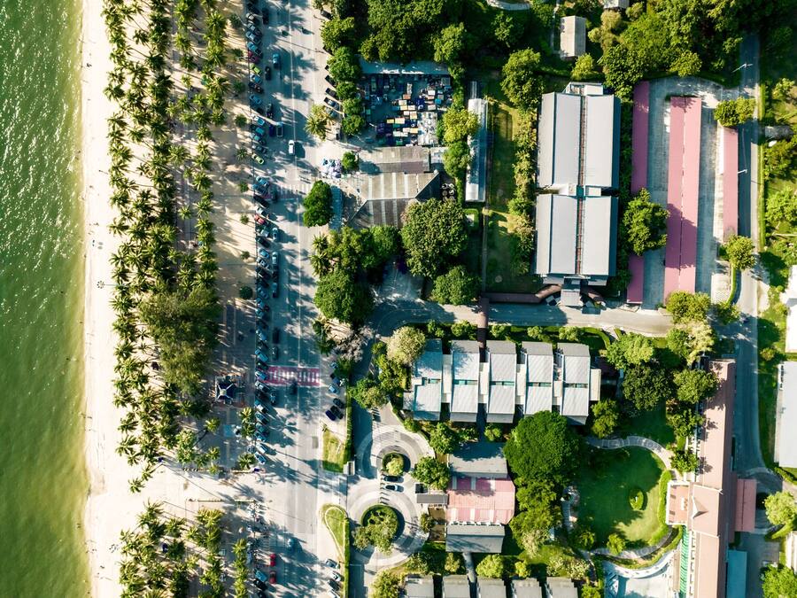 Vue aérienne d’une zone côtière avec une plage, des parkings et des bâtiments.