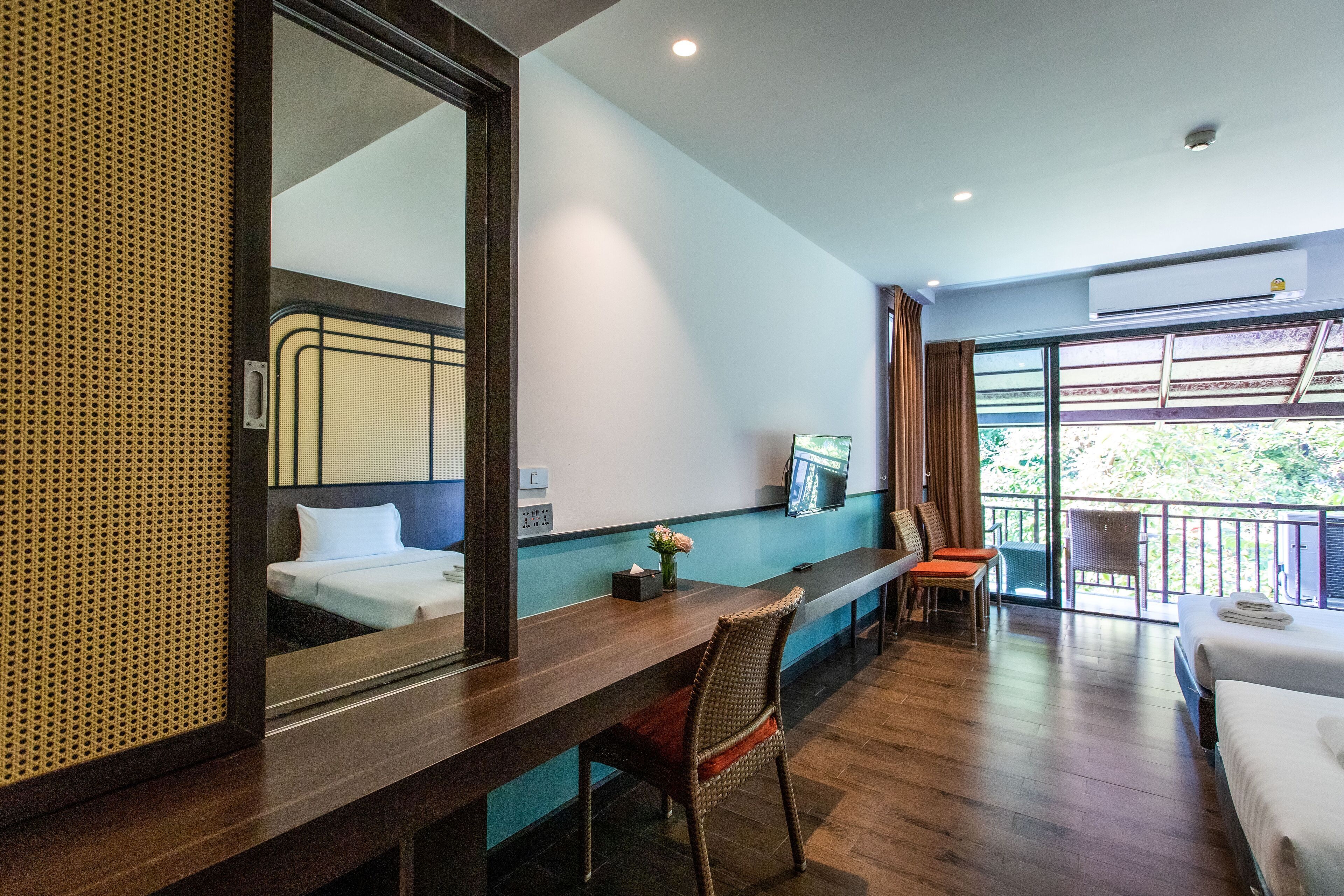 Habitación de hotel con escritorio de madera, una silla, cama, televisor y balcón con vistas.