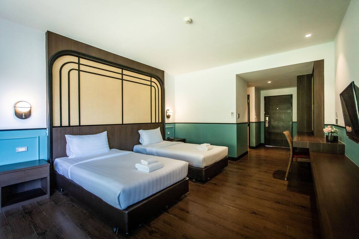 Une chambre d’hôtel avec deux lits, un plancher en bois, une grande fenêtre et un bureau avec une chaise.