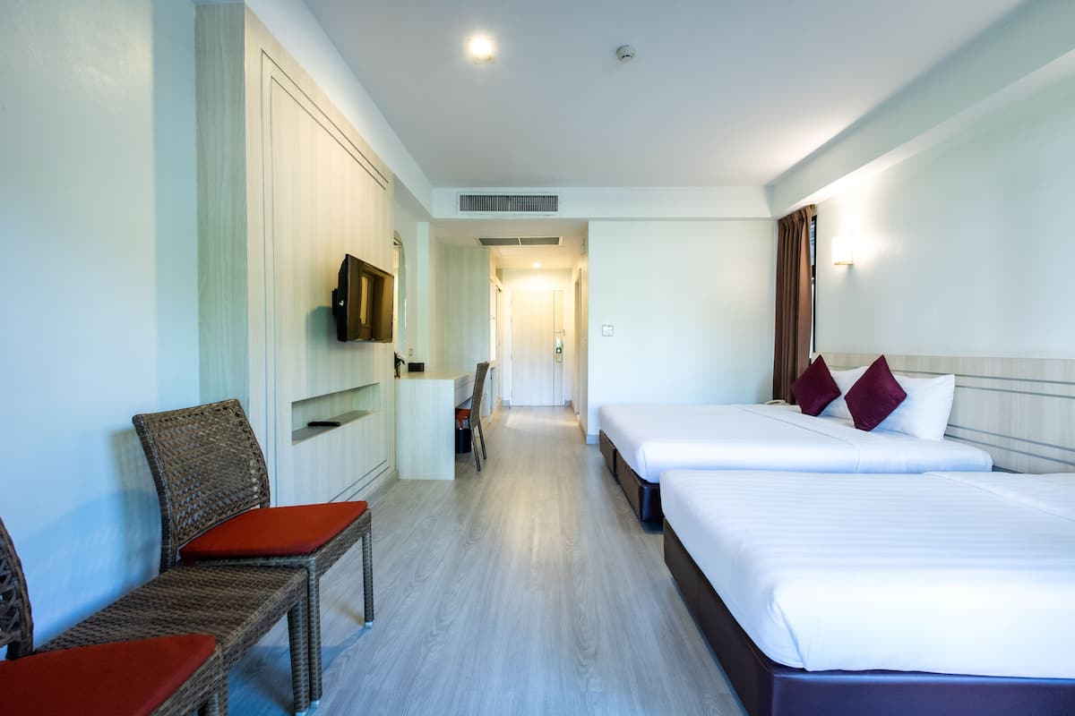 Une chambre d’hôtel avec deux lits, un téléviseur fixé au mur, un coin salon avec des fauteuils et un couloir menant à une autre chambre.