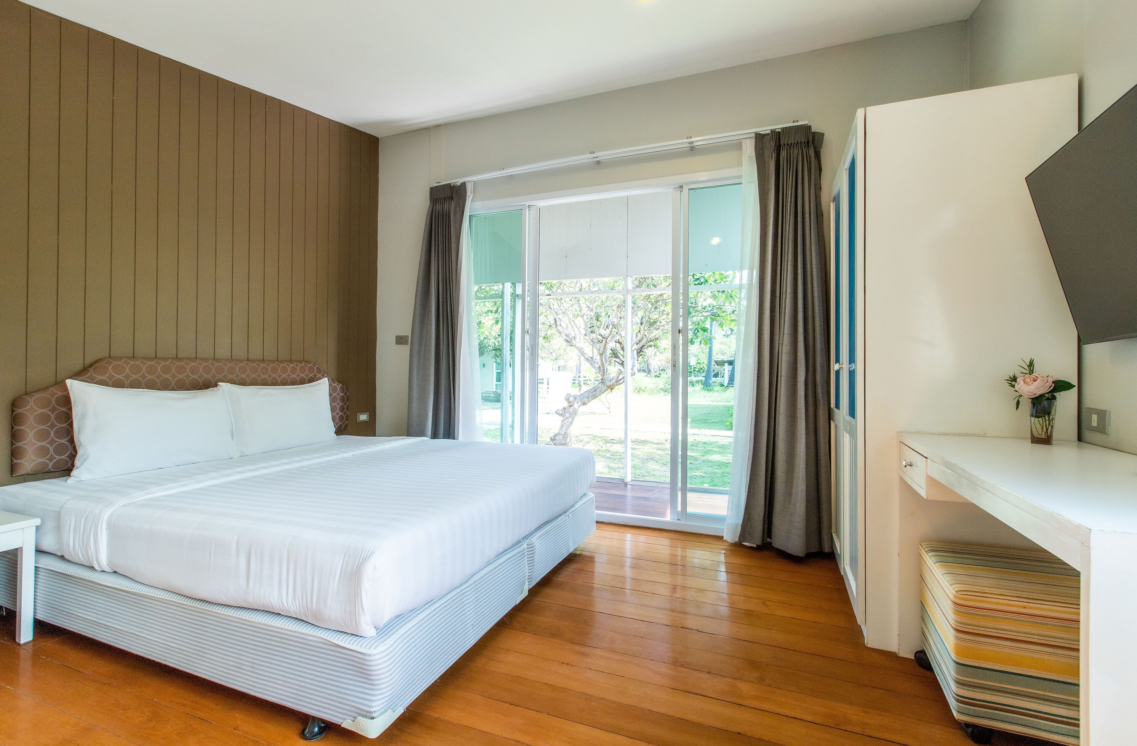 A bedroom with a large bed, a desk, and a sliding glass door leading to a balcony.