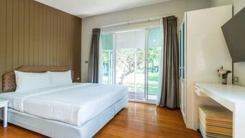 A bedroom with a large bed, a desk, and a sliding glass door leading to a balcony.