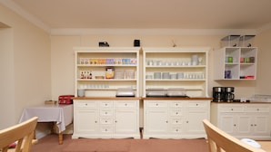 Una cocina con armarios blancos, una mesa con mantel y diversos utensilios de cocina en los estantes.