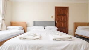 Habitación de hotel con dos camas individuales, una cama doble grande, una puerta de madera y un radiador.