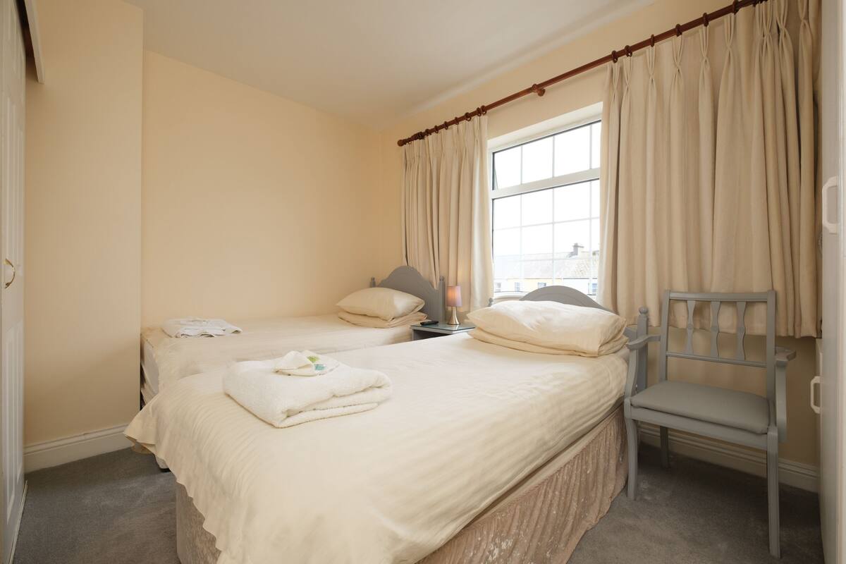 A bedroom with two beds, a chair, and a window with curtains.