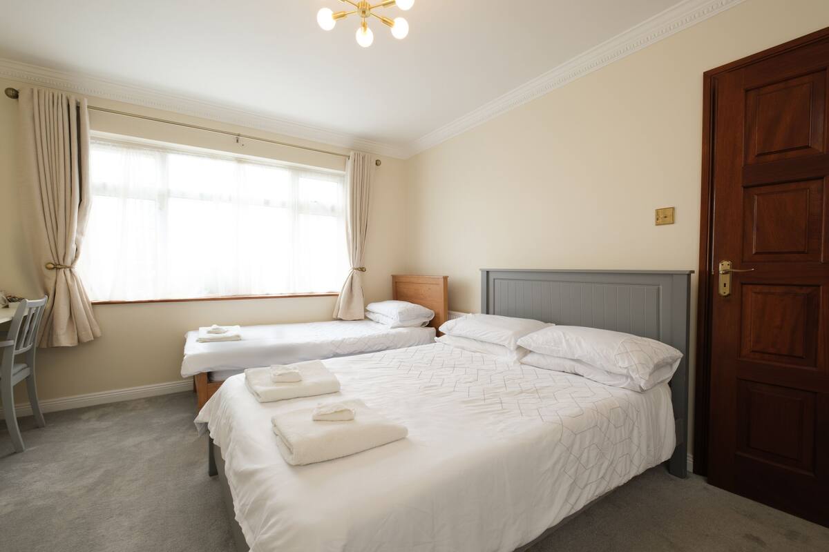 A hotel room with two beds, a desk, and a large window with curtains.