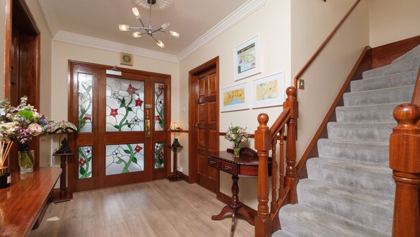 Una escalera de madera con un rellano alfombrado, un escritorio de madera y un jarrón de flores.