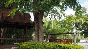 A traditional wooden structure with a sign in a foreign script, surrounded by lush greenery and a large tree. - Phutawan Kan Resort (Kanchanaburi)