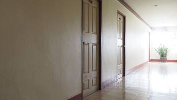 Um corredor com duas portas, uma delas com a placa '101' e a outra '102', dando acesso a quartos. O corredor possui um piso de azulejos e um vaso de plantas no canto.