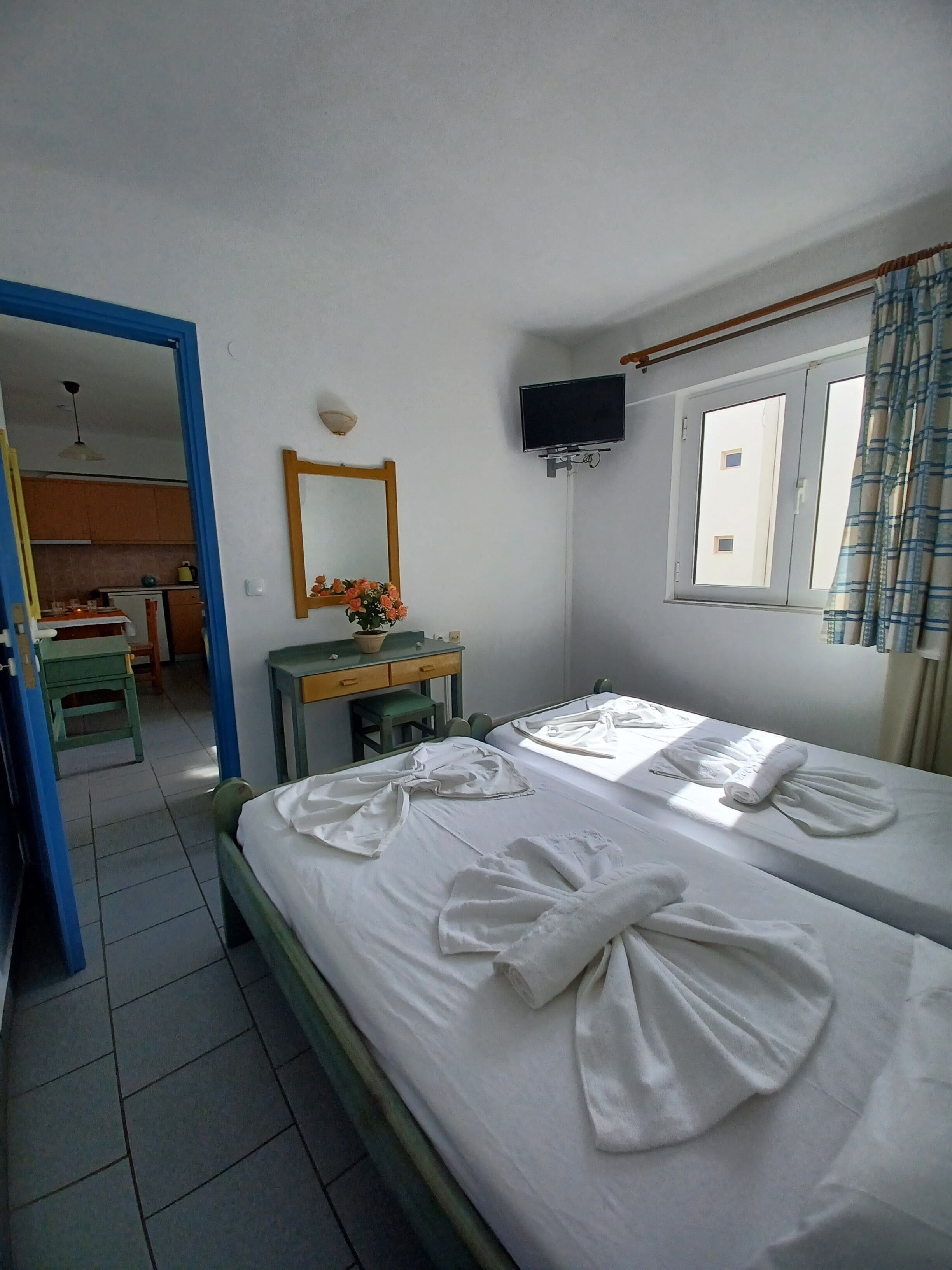 A hotel room with two beds, a desk with a chair, a mirror, a TV, and a window with curtains.