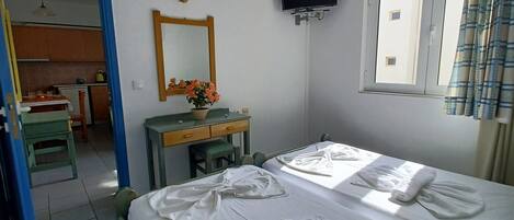 A hotel room with two beds, a desk with a chair, a mirror, a TV, and a window with curtains.