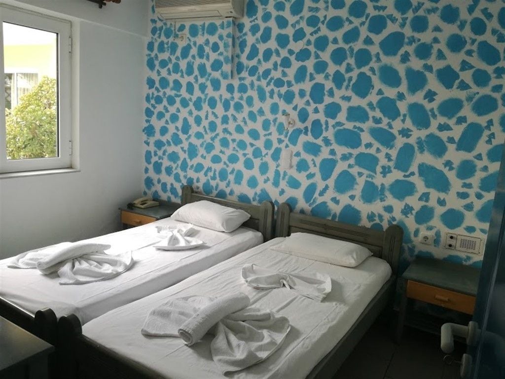 Una habitación con dos camas, una ventana y un papel tapiz estampado.