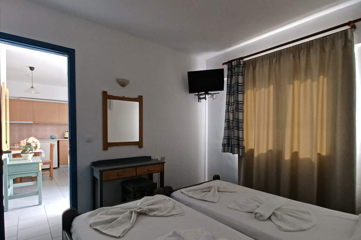 A hotel room with two beds, a desk, a chair, a flat-screen TV, and a bathroom visible through an open door.