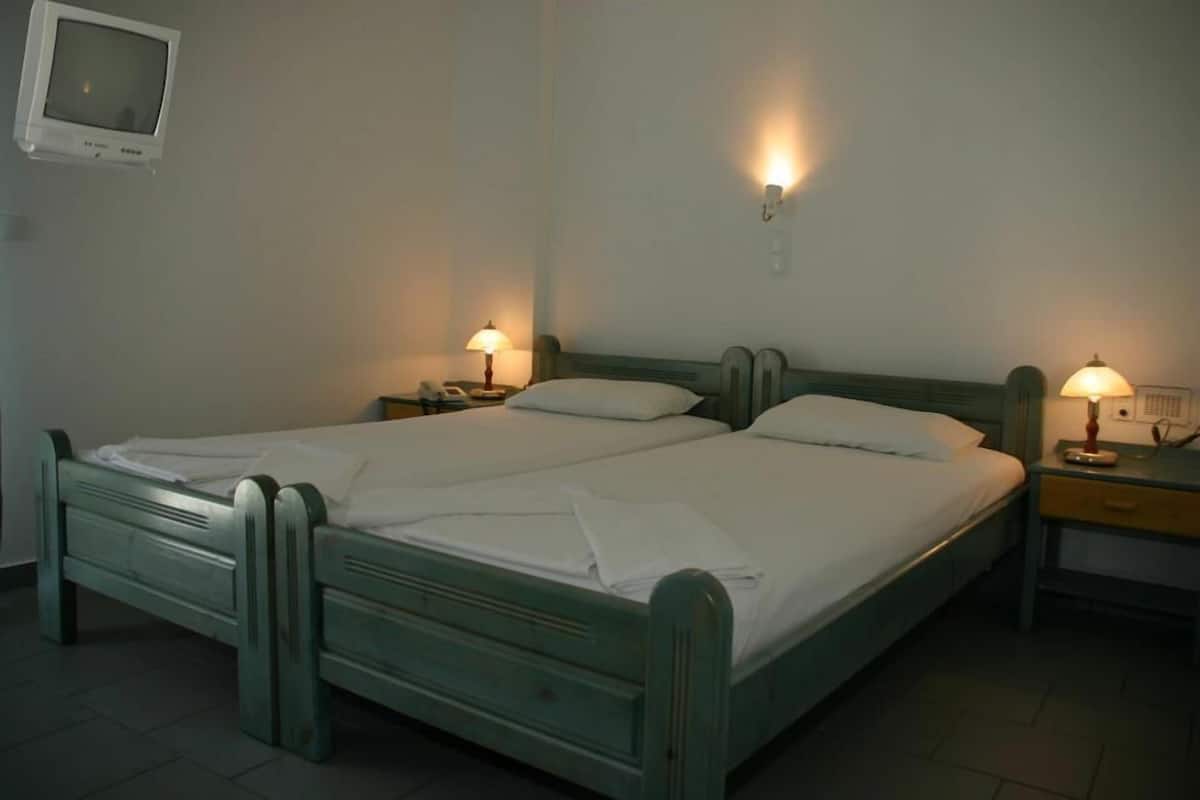 A double bed with a wooden frame, two bedside tables with lamps, and a small television mounted on the wall.