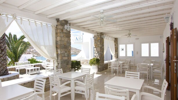 Un espacio de comedor al aire libre con decoración blanca, pilares de piedra, mesas y sillas blancas, con vistas a la costa.