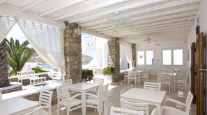 A white-themed outdoor dining area with stone pillars, white tables, and chairs, overlooking a coastal view.