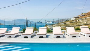 Zona de piscina con sillones de descanso y vistas al mar y un crucero.