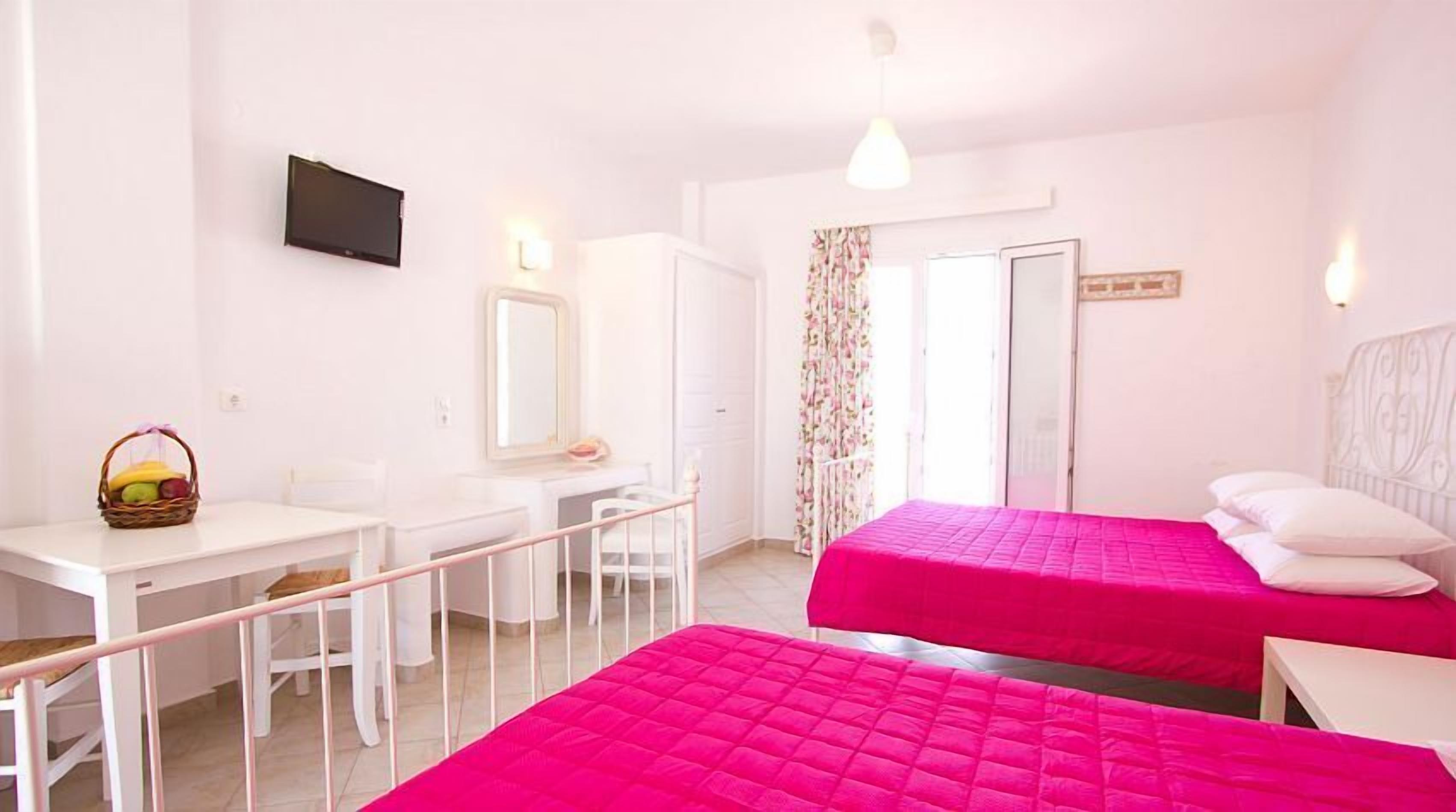 A bedroom with two beds, a desk, a chair, a mirror, and a television on the wall.