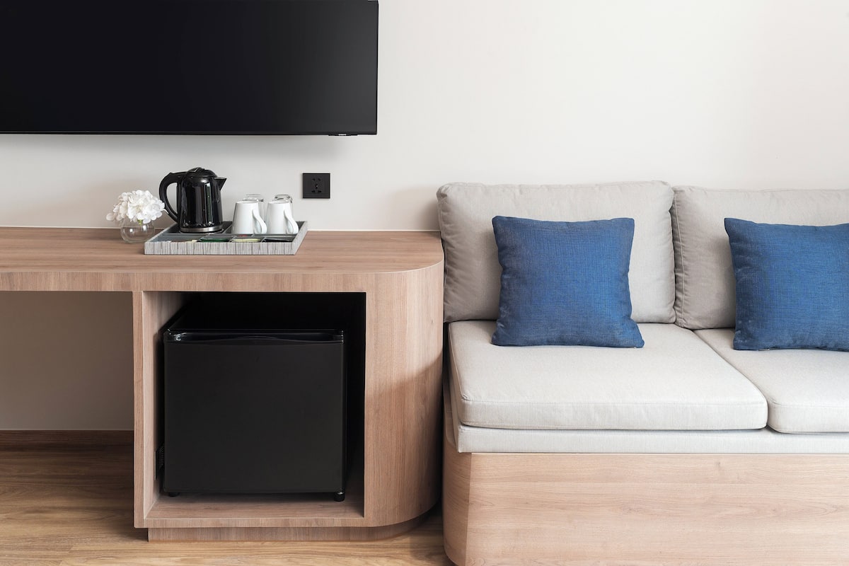 Una sala moderna con una consola de madera, un refrigerador negro, un televisor de pantalla plana y un sofá de color claro con cojines azules.