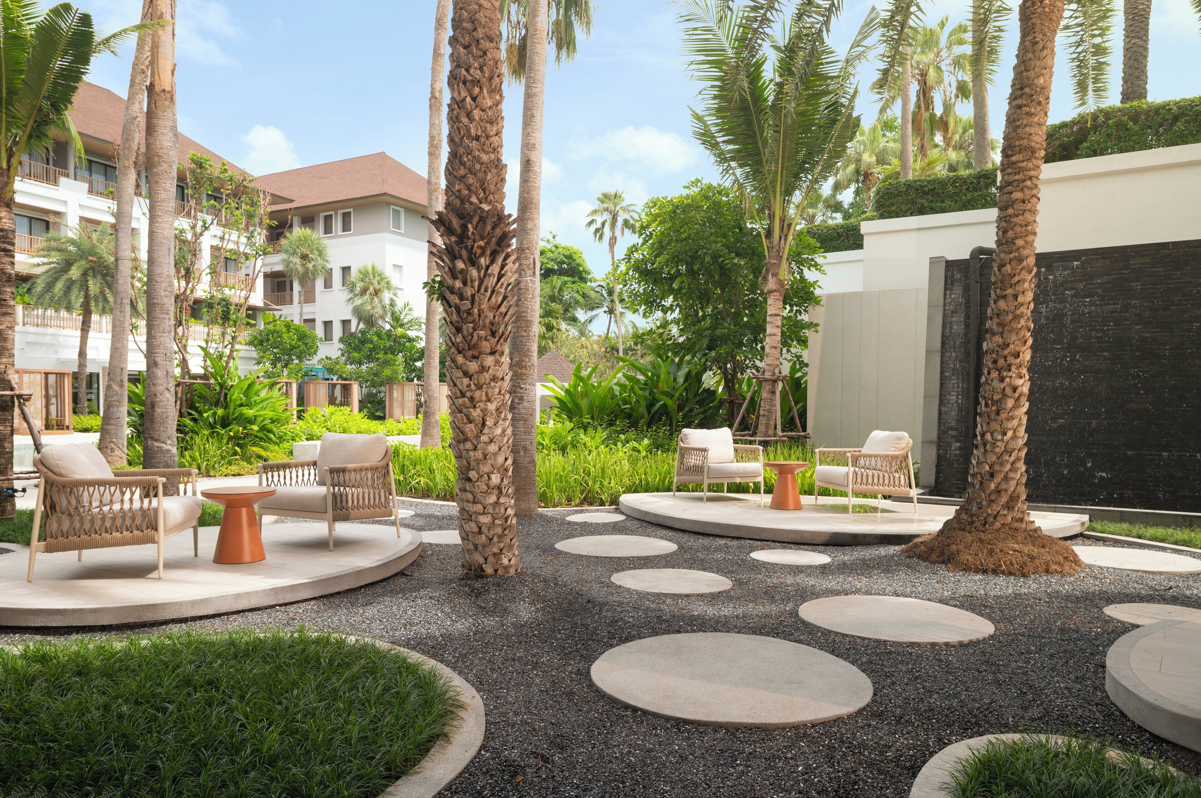 Une cour d’hôtel avec des espaces de détente en plein air, des palmiers et un espace piscine.