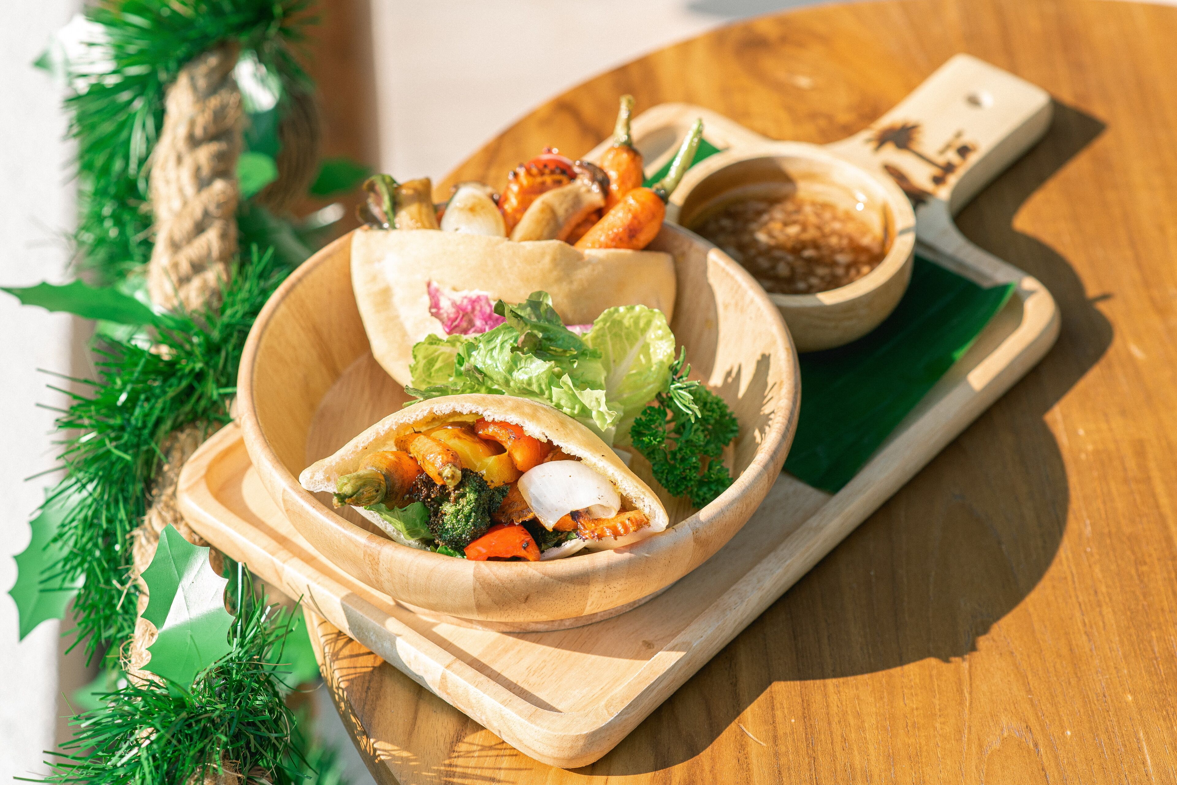 A wooden serving tray with a bowl of food, including a wrap and a bowl of sauce, on a wooden table.