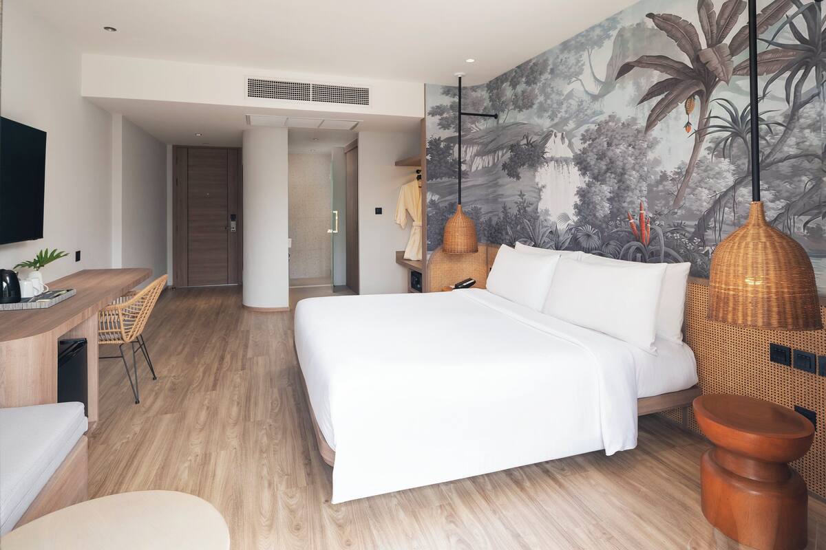 Una habitación de hotel moderna con una cama grande, un escritorio con una silla, un televisor y un mural con una escena tropical.